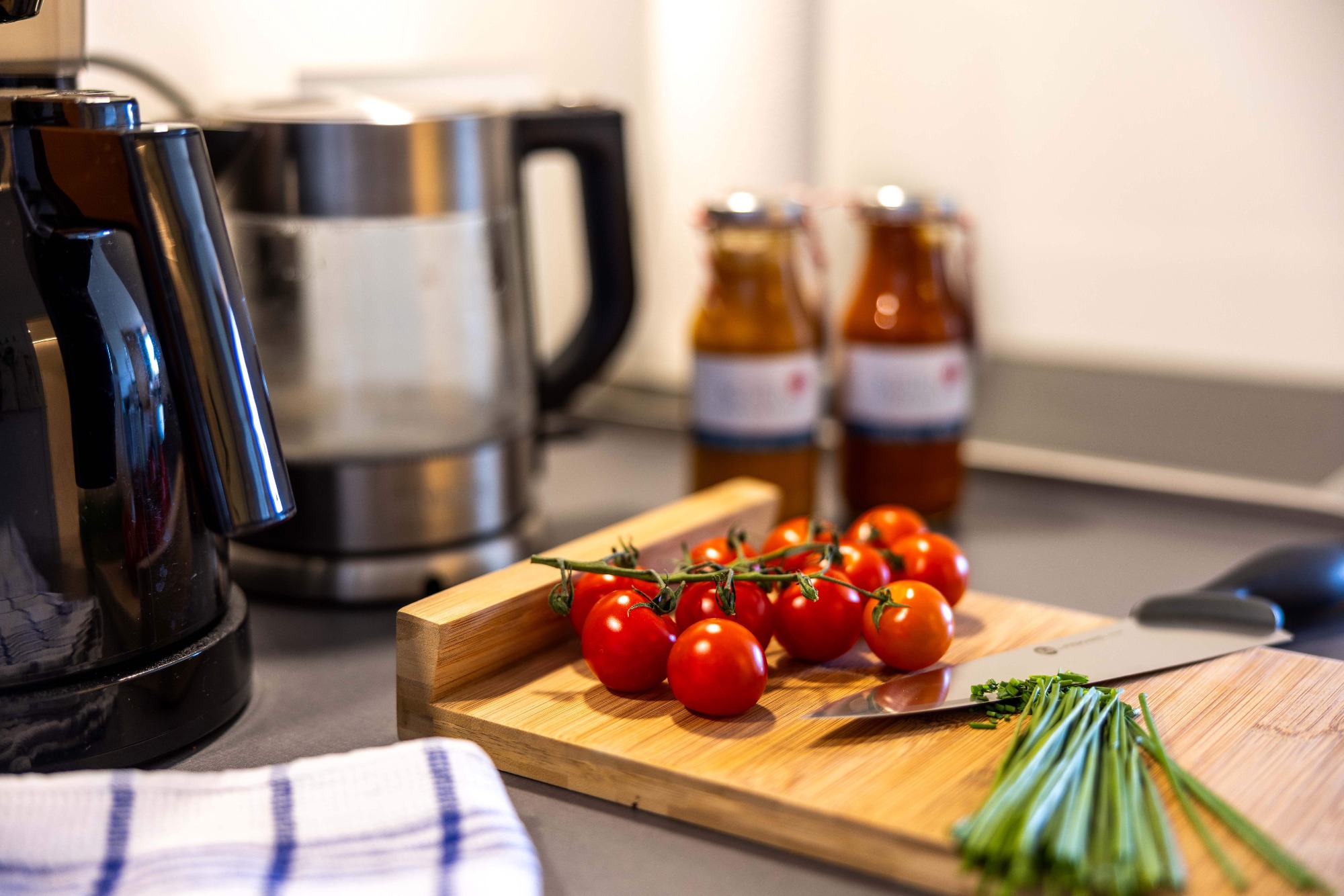 Seeluft macht hungrig ! Frische Tomaten und Schnittlauch auf einem Holzbrett, daneben eine Wasserkocher und zwei Flaschen.