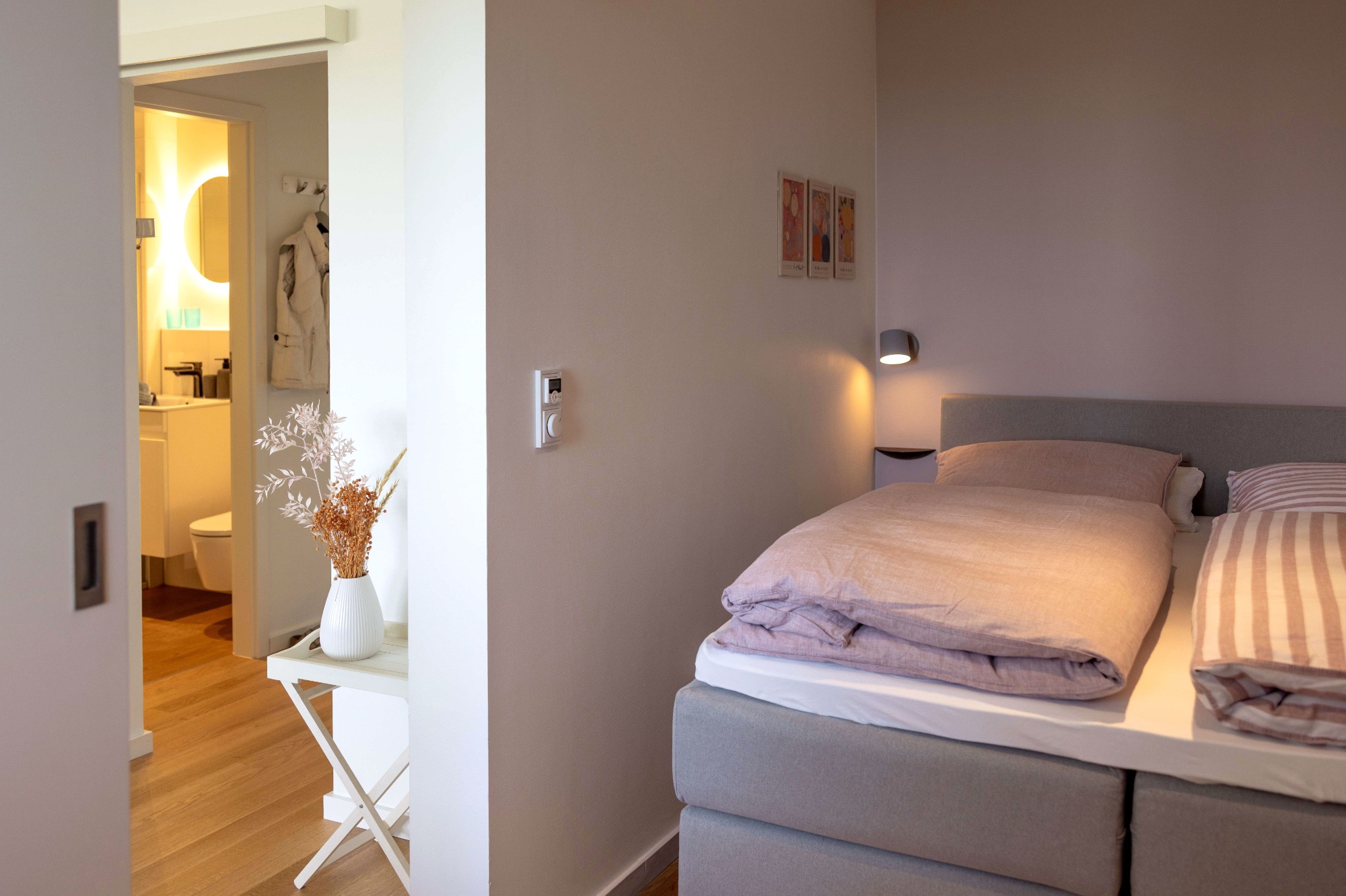 So eine gemütliche Koje Helles Schlafzimmer mit einem Bett, beleuchtetem Nachttisch und Blick auf ein Badezimmer.