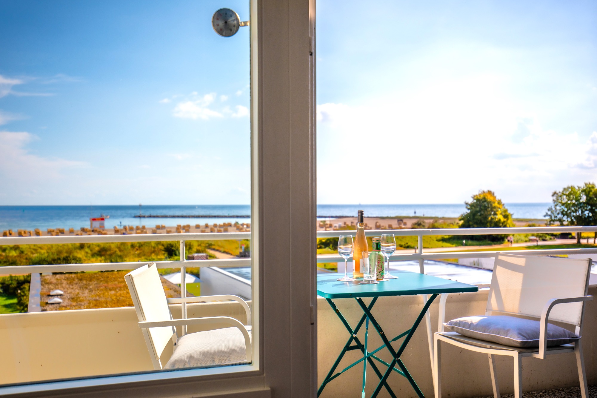 Windgeschützter Sonnenbalkon Blick auf den Strand von einer Terrasse mit einem Tisch und einem Getränk.