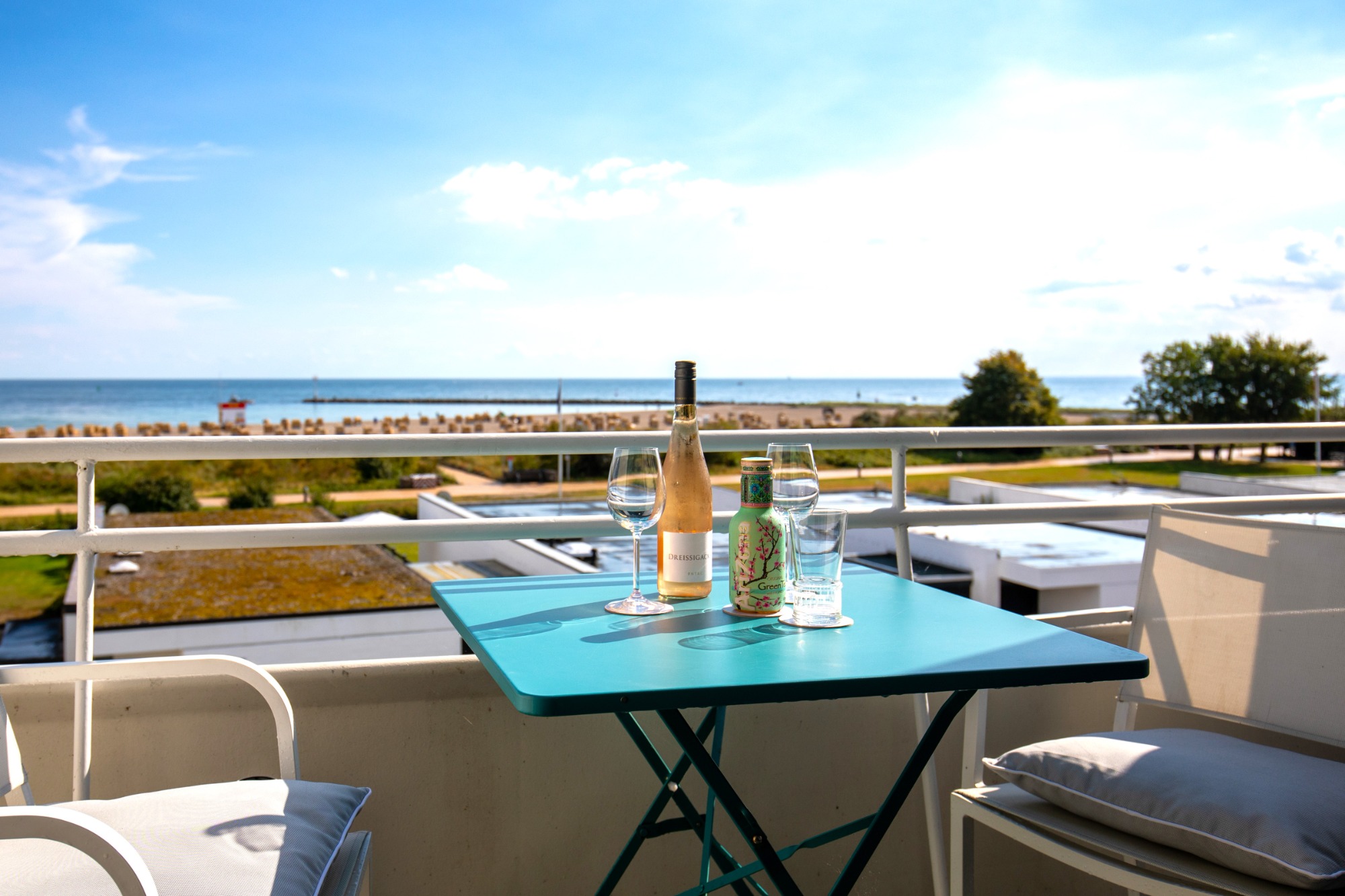 Fernsicht 180° Süd Tisch auf Balkon mit Weinflasche und Gläsern, Blick auf das Meer und den Himmel.