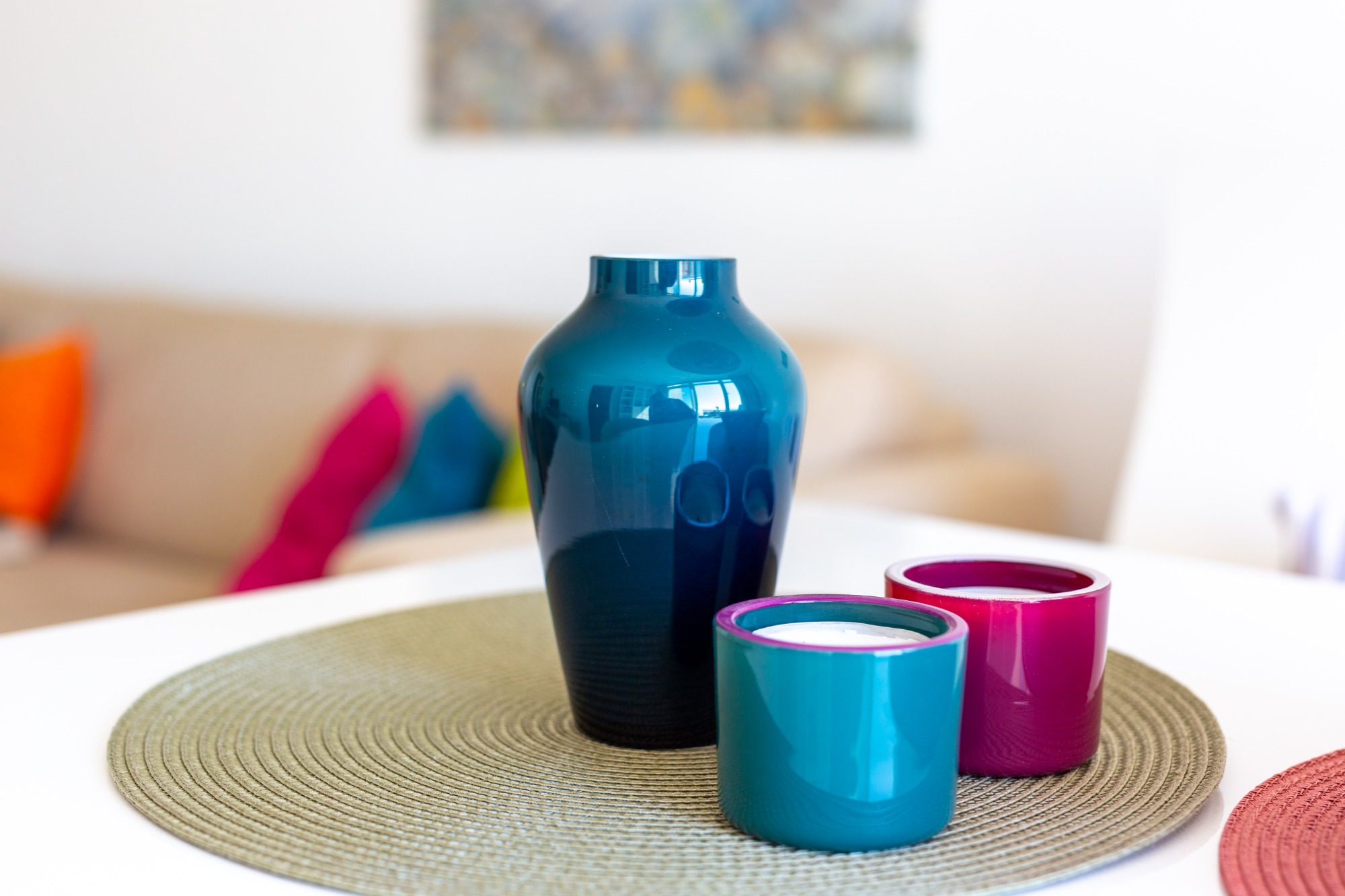 Frische Farben Blauer Vase mit zwei bunten Bechern auf einem runden Tisch in einem hellen Raum.