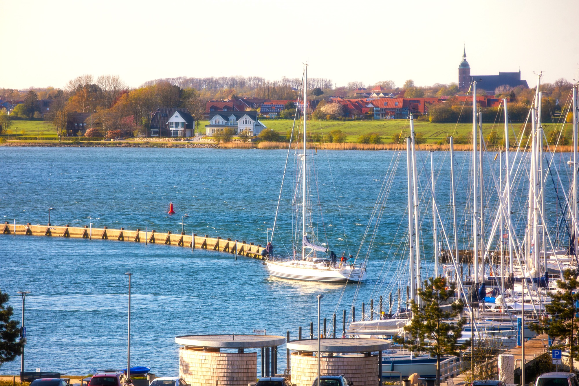 Anlegemanöver geglückt ? Segelboot fährt in den Hafen, umgeben von Yachten und einer weiten grünen Landschaft.