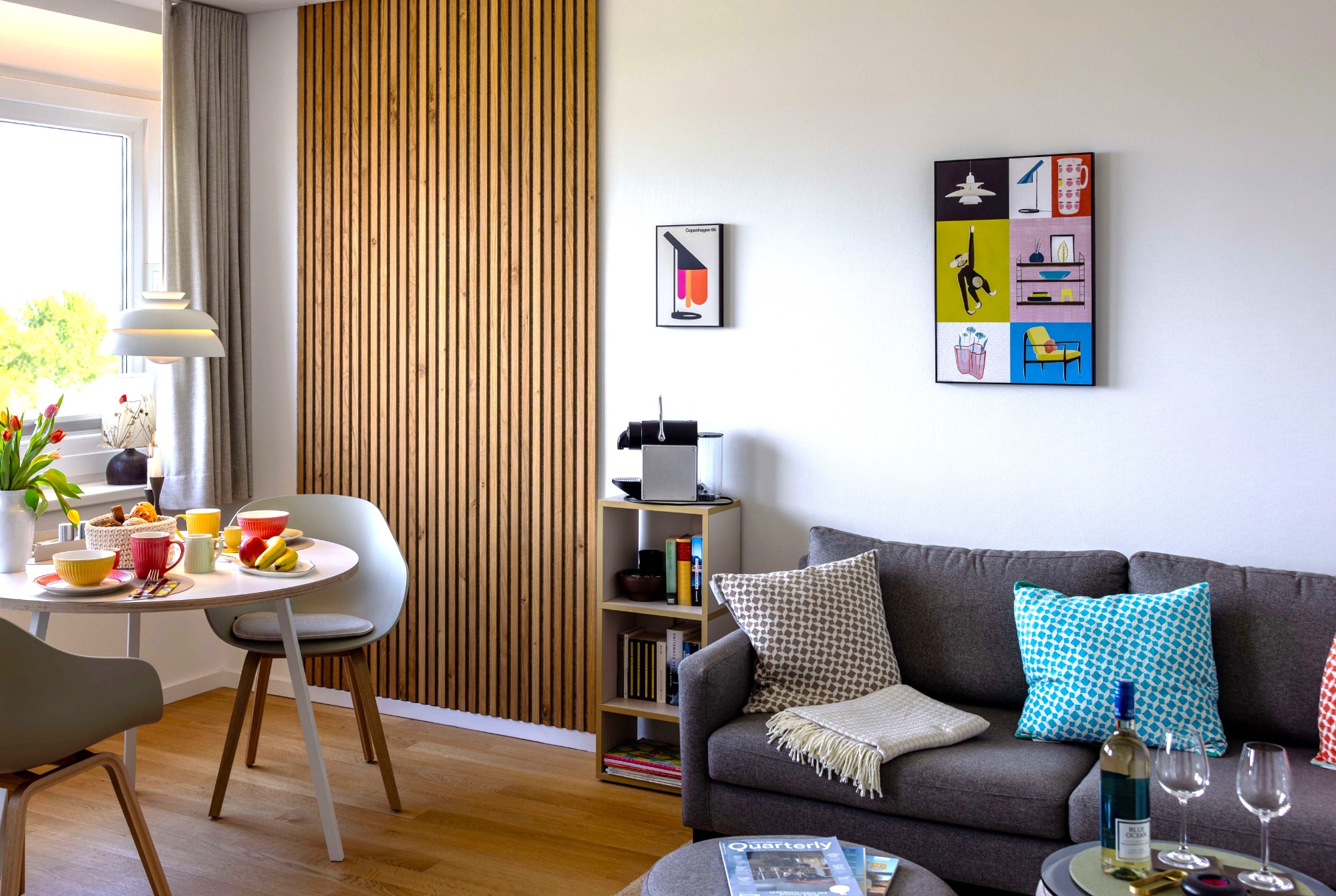 Helle Einrichtung, warme Farben ... Helles Wohnzimmer mit Sofa, Esstisch, Pflanzen und bunten Wandbildern.