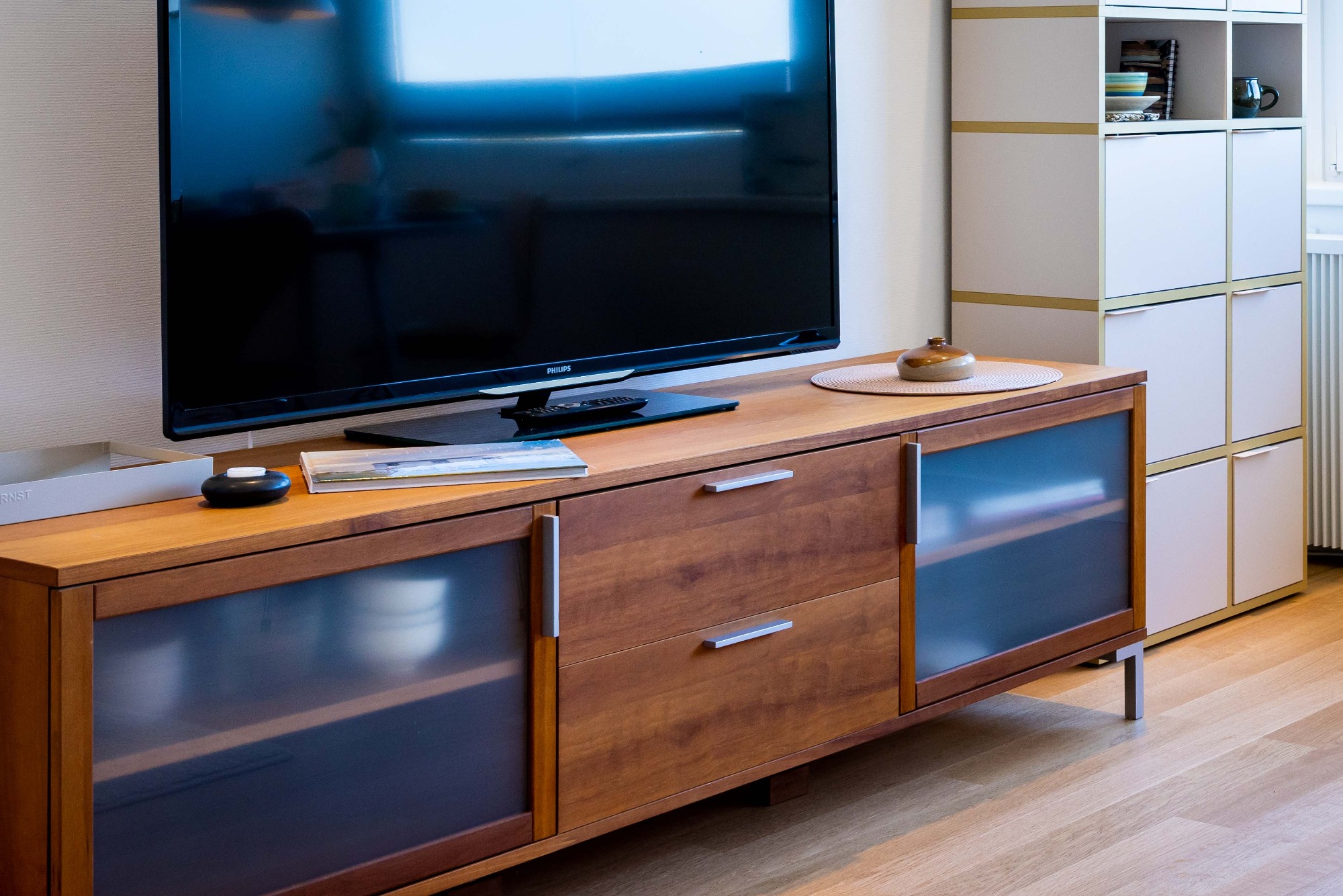 Klare Linien Holzfernsehmöbel mit Glastüren, Fernseher und Regalelement im Hintergrund.