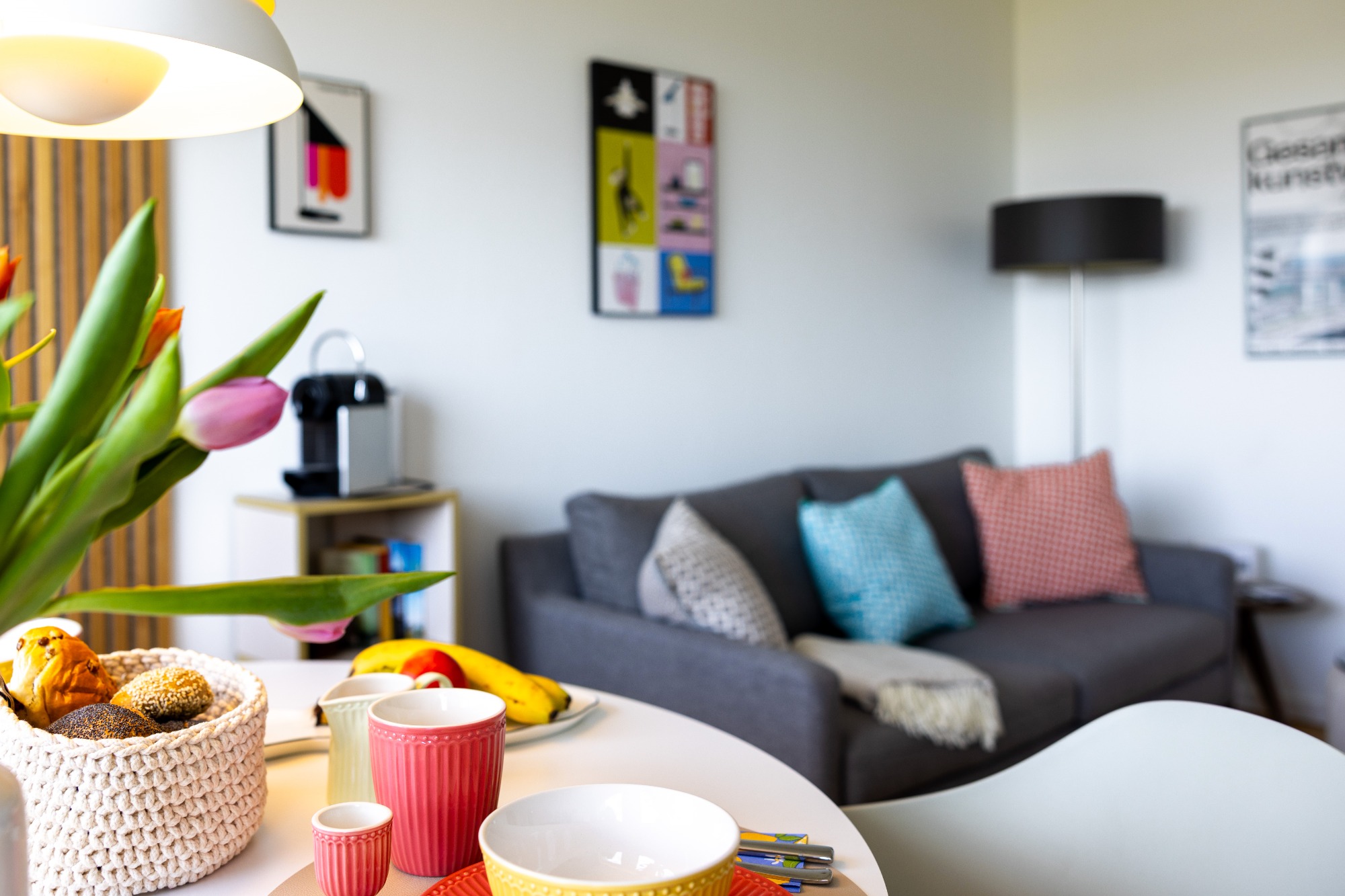 Großer Wohnraum Moderne Wohnstube mit grauem Sofa, bunten Kissen und Esstisch mit Obst und Blumen.